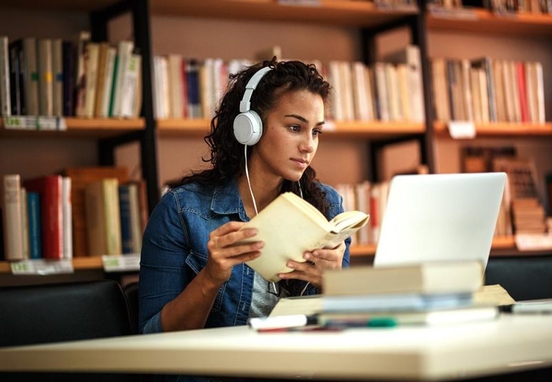 Female-student-reading-and-studying-at-laptop-in-library 800px x 451px